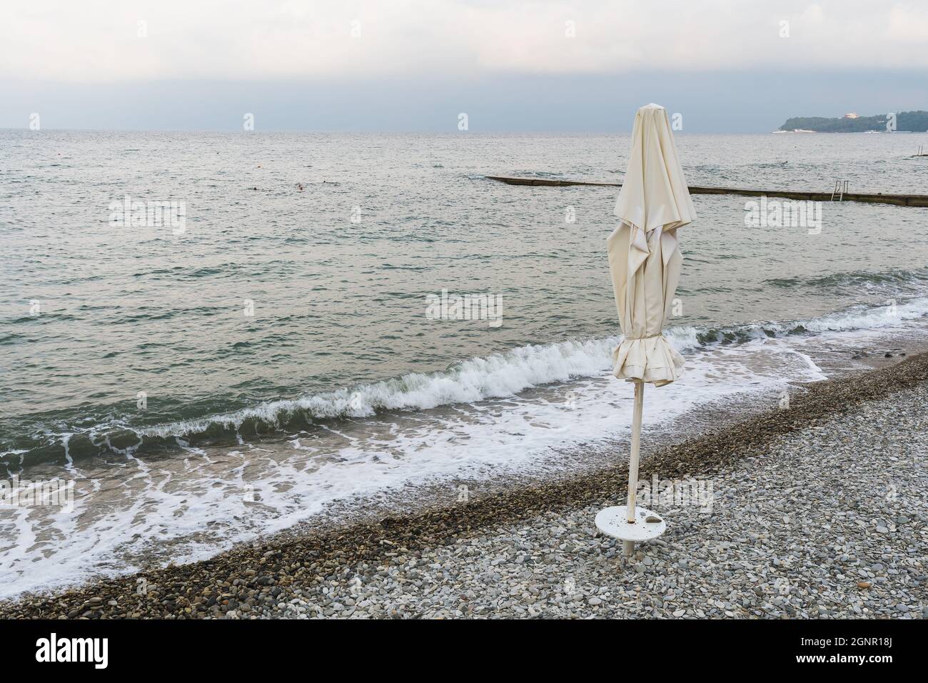 Tempesta in mare, spiaggia di ciottoli vuota e ombrello chiuso Foto Stock