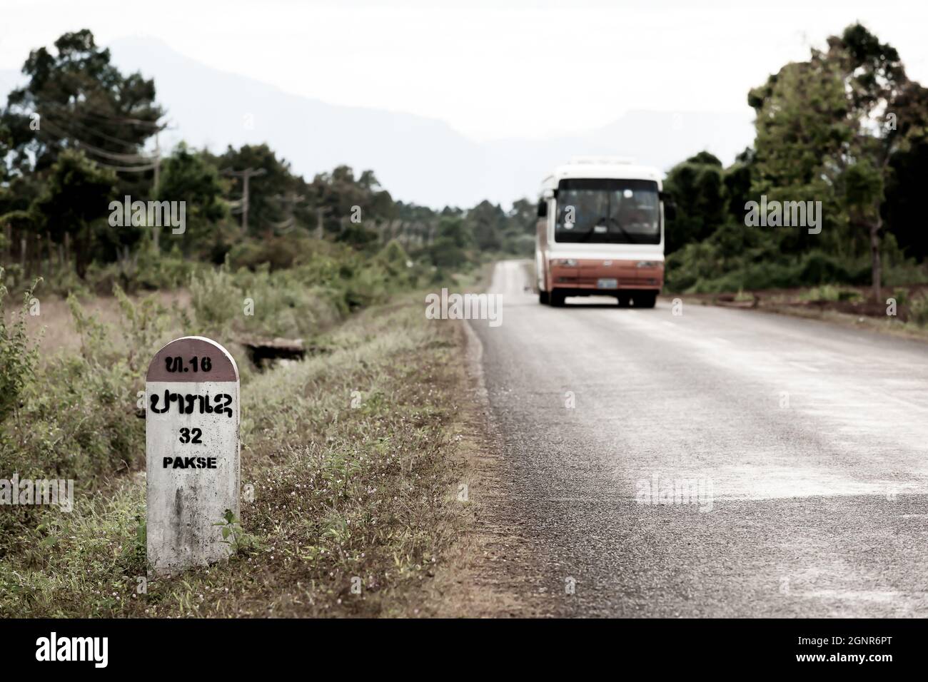 Cartello Laos Milestone sull'autostrada nazionale T 16, che indica 32 chilometri per Pakse da Salavan vicino al confine con il Vietnam. Un autobus locale offuscato sulla strada. Foto Stock