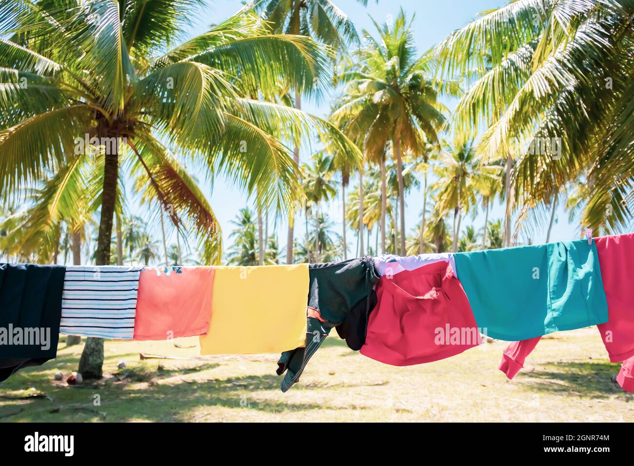 Abiti per bambini appesi sulla linea di vestiario in un giardino di cocco al mare durante l’estate soleggiata. Foto Stock