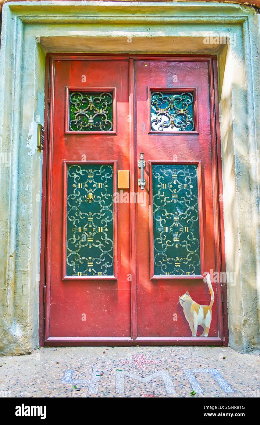 ODESSA, UCRAINA - 18 giugno 2021: La porta rossa coniata con griglie in ghisa ornata e il gatto dipinto, il 18 giugno a Odessa Foto Stock