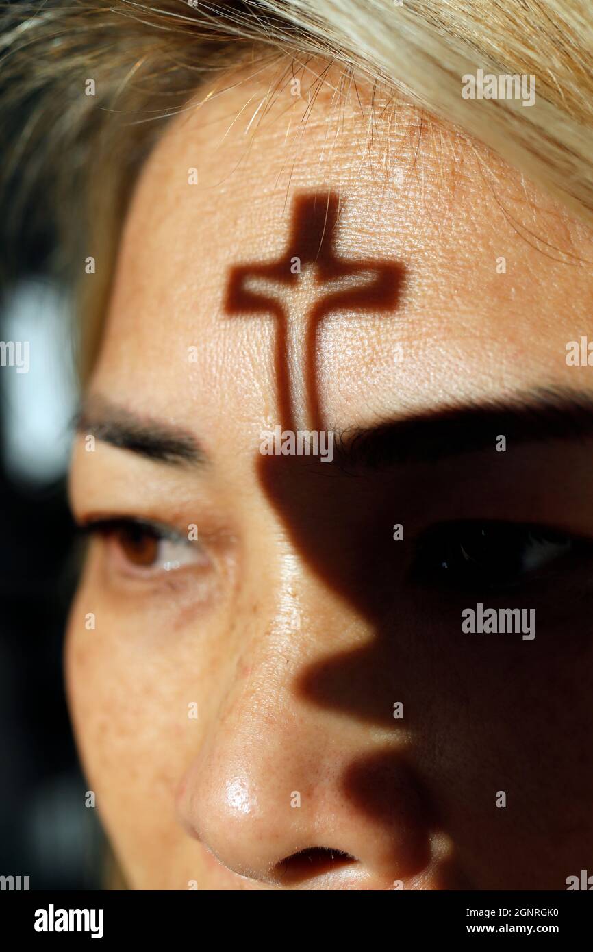 Ombra di un piccolo crocifisso sul volto di una donna cristiana. Fede e religione. Foto Stock