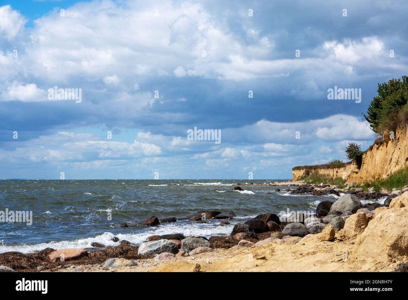 Costa ripida con spiaggia sabbiosa e massi sul Mar Baltico in una giornata estiva con cielo blu e nuvole Foto Stock