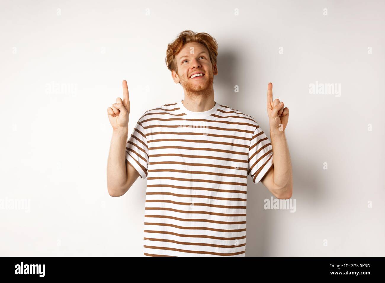 Buon giovane uomo con capelli rossi e la barba puntata, guardando in su con il sorriso sognante, controllando l'offerta speciale promo, sfondo bianco. Foto Stock