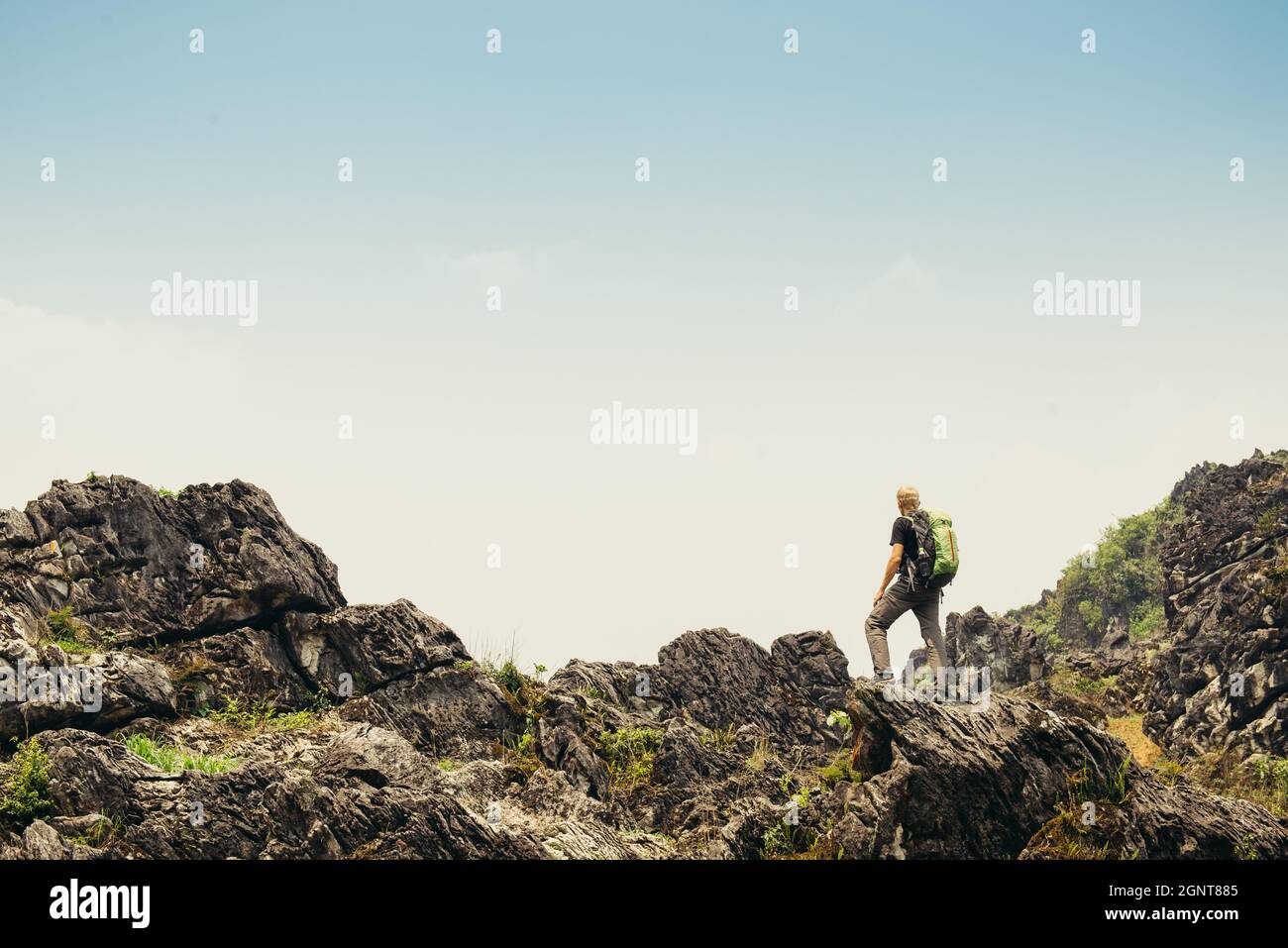 Uomo a piedi con zaino in alto nelle verdi montagne in estate. Osservazione del paesaggio durante una breve pausa. Spazio di copia sul cielo limpido in Vietnam Foto Stock