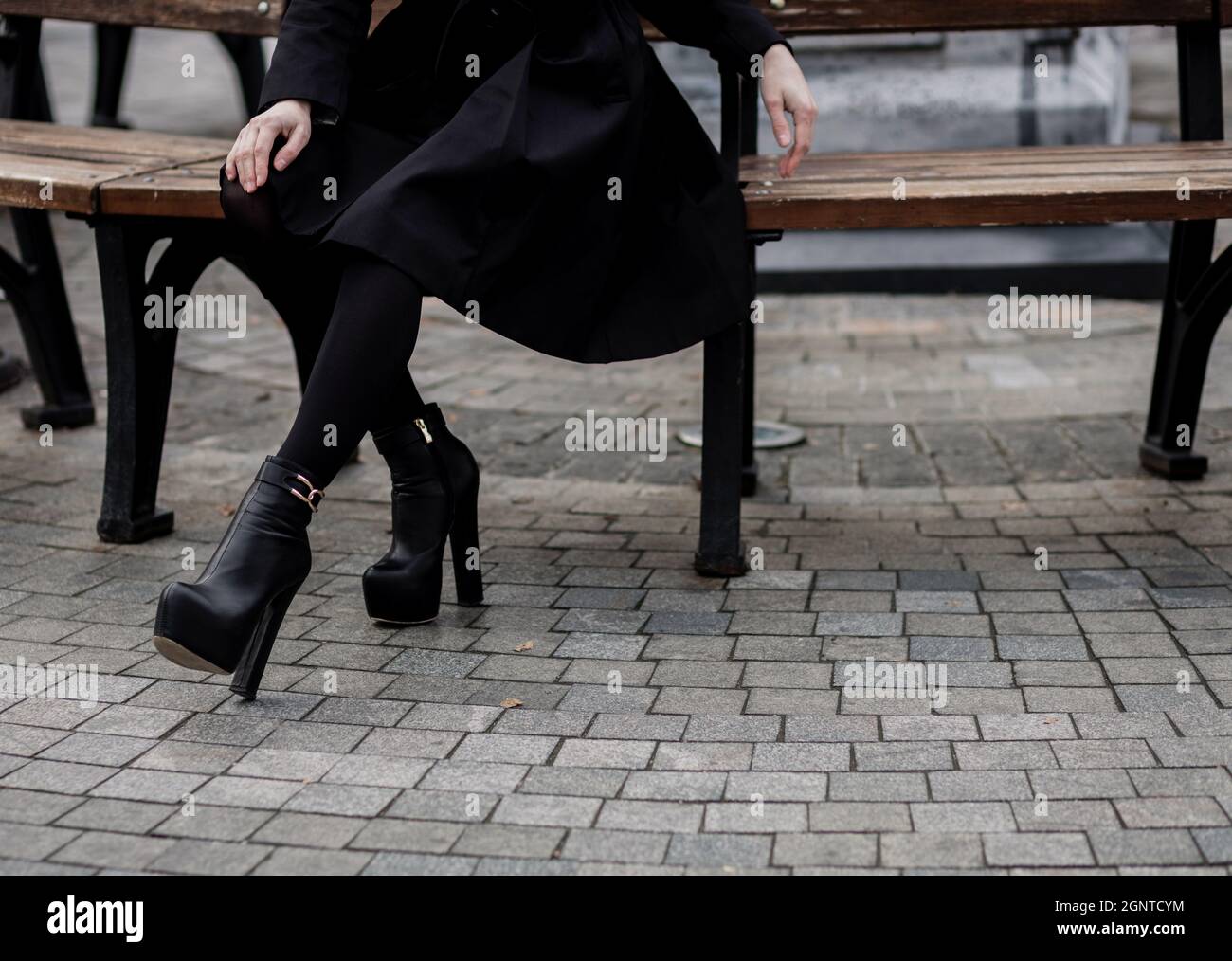 Donna che indossa cappotto nero e stivali in pelle e seduta su panca.  Abbigliamento casual alla moda. Dettagli del look di tutti i giorni Foto  stock - Alamy