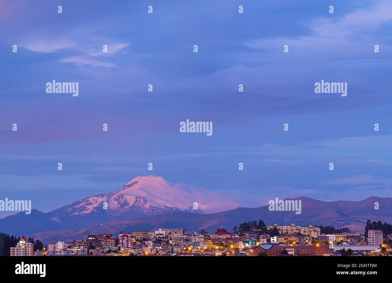 Città di Quito al tramonto durante l'ora blu con il vulcano Cayambe, Ecuador. Foto Stock