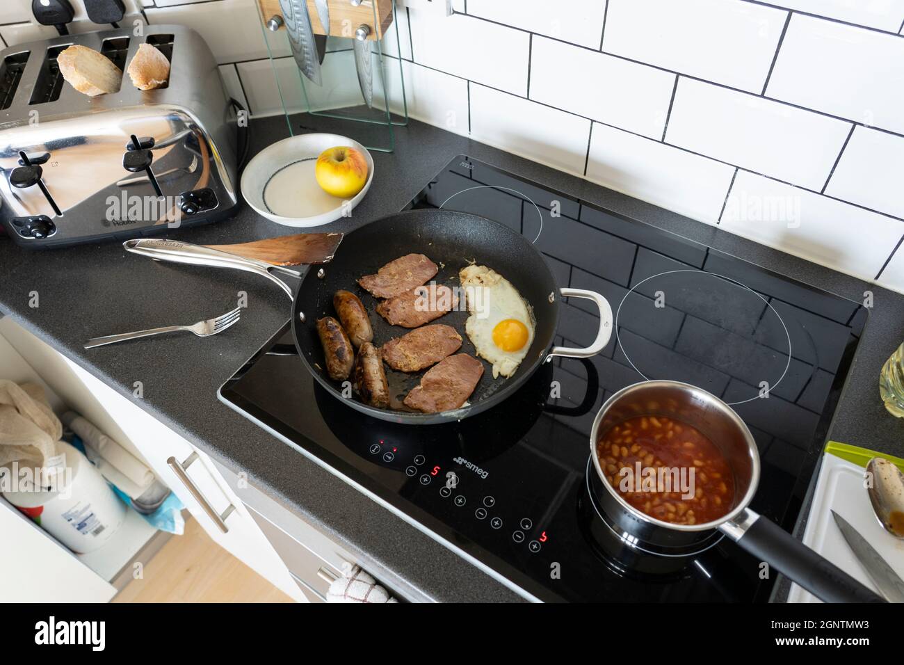 Colazione inglese tradizionale in una cucina con uova fritte, affettati di pancetta e salsicce che cucinano in una padella, e fagioli cotti in una padella. Inghilterra Foto Stock