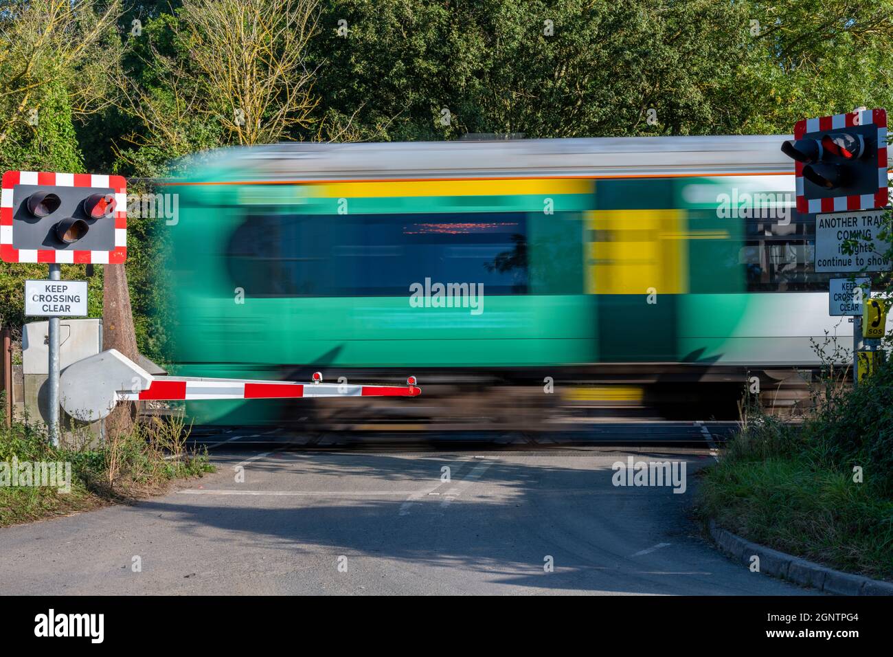 un treno che passa su un incrocio a livello nel sussex ovest. a livello ferroviario che attraversa una strada con luci rosse lampeggianti per l'attraversamento della sicurezza in sussex. Foto Stock