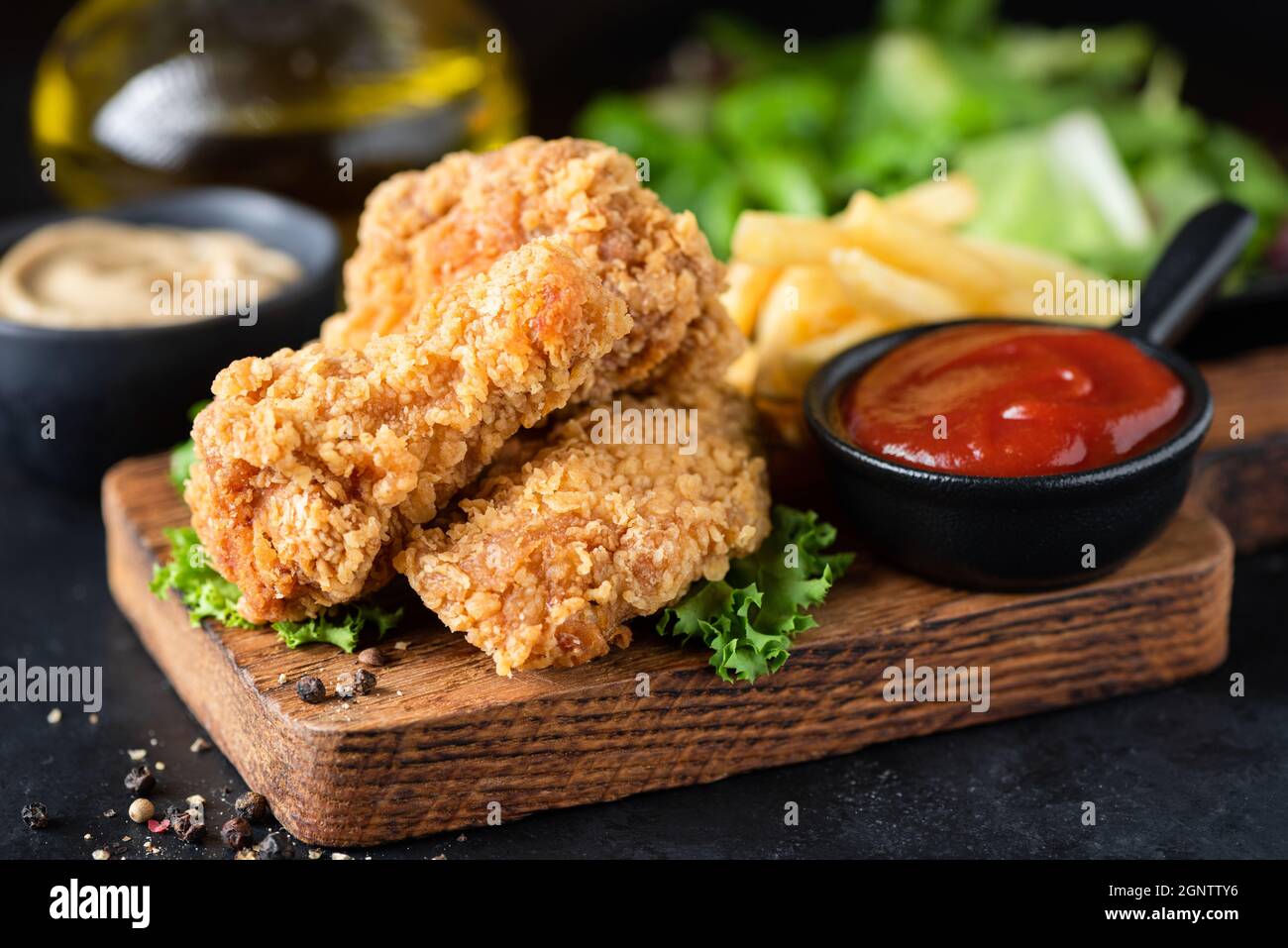 Ali di pollo fritte, fritte francesi e Ketchup su tavola di servizio in legno, vista Closeup Foto Stock