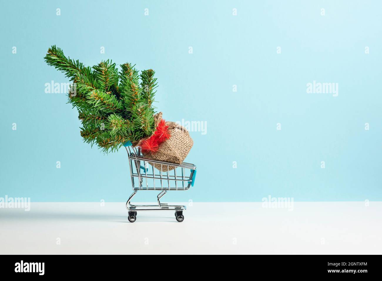 Albero di Natale in un carrello di shopping da un supermercato isolato su sfondo azzurro chiaro. Nuovo anno o concetto di vendita di Natale. Banner con spazio di copia Foto Stock