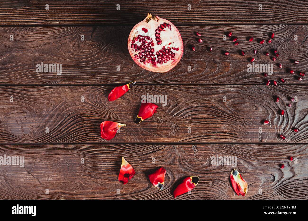 Vista dall'alto di un melograno tagliato a metà con semi sparsi e petali di fiori su un tavolo di legno marrone. Foto Stock