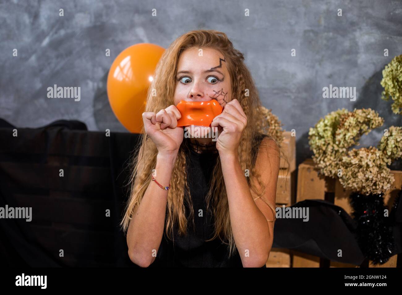 Adolescente ragazza con capelli shaggy gonfia arancione scoppio gonfiabile pallone tra decorazione su Halloween Foto Stock