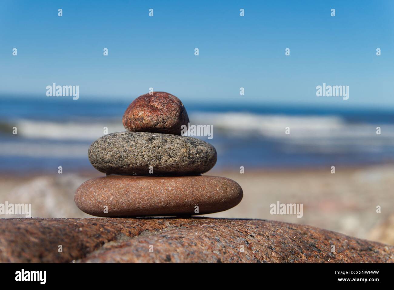 Accatastato di pietre o rocce su una spiaggia posta sulla cima di un masso che si affaccia sull'oceano e dolci onde Foto Stock