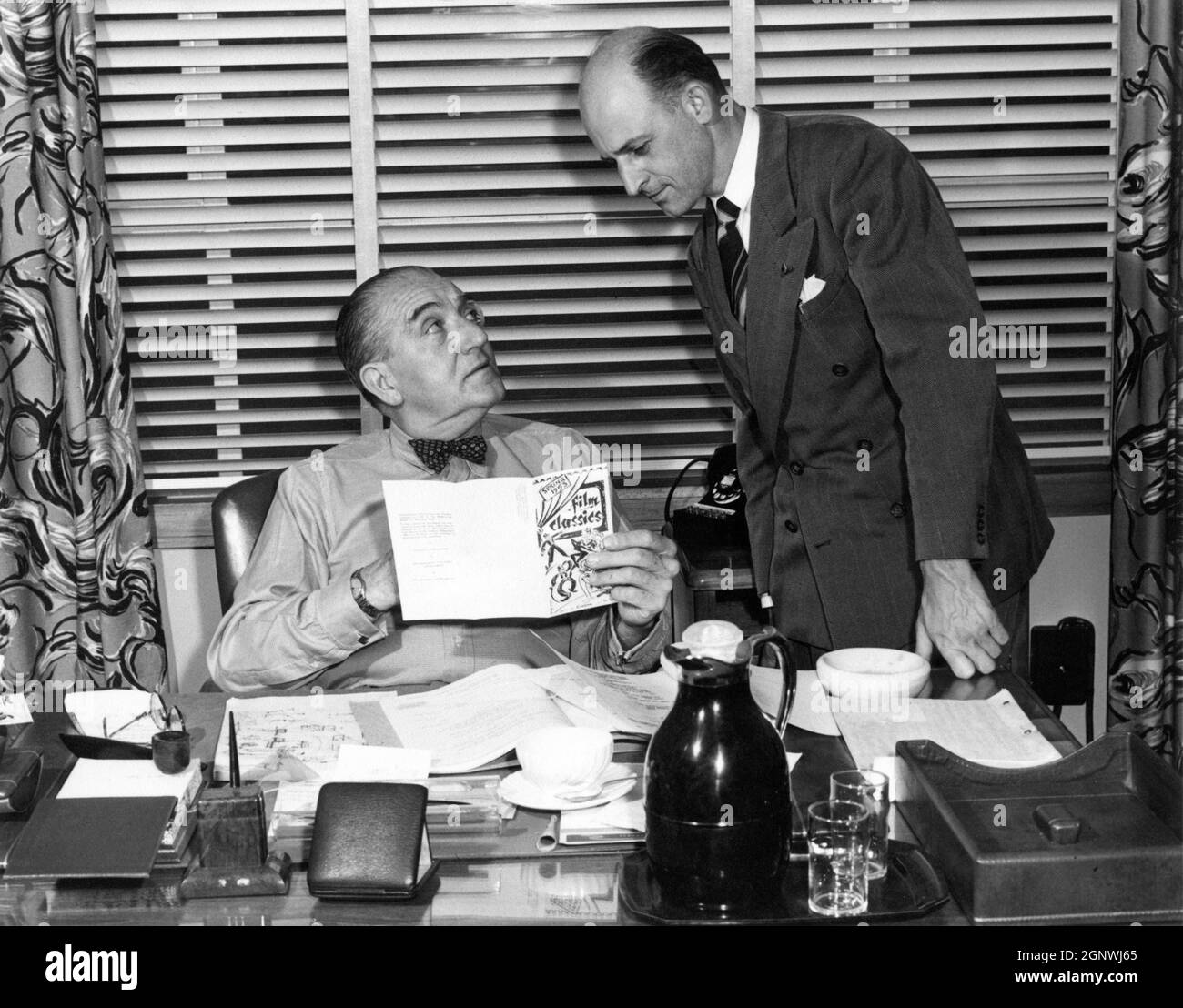 FRITZ LANG nel suo ufficio presso i Columbia Studios nel febbraio 1953 al momento in cui stava facendo IL GRANDE CALORE con LARRY COURTNEY mostrargli un programma per la Primavera 1953 Film Classics presumibilmente compreso un film di Fritz Lang Foto Stock