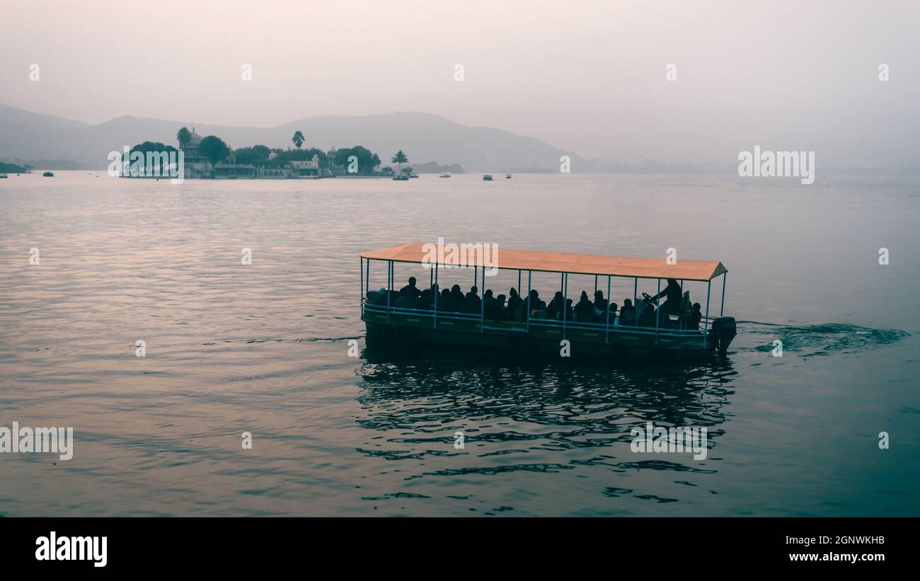 Una barca di colore arancione sul lago blu di Pichola durante la luce del giorno a Udaipur, Rajasthan Foto Stock