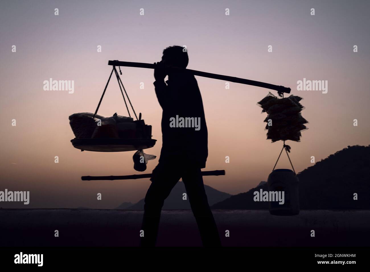 Silhouette di un venditore di strada che porta tutto sulla sua spalla durante il tramonto a Udaipur, Rajasthan Foto Stock