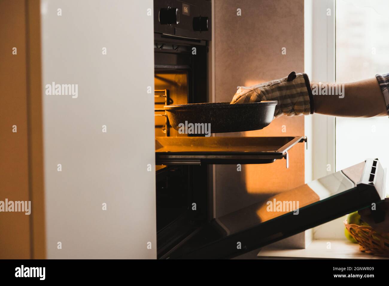 La mano dell'uomo in potholder mette la muffa con il piatto nel forno incorporato in cucina a casa. Chiudere lo sportello e premere il pulsante. Primo piano. Foto Stock