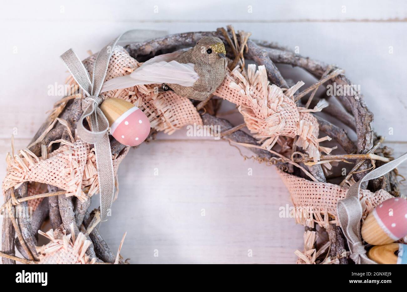 Corona pasquale fatta a mano, fatta di rametti e nastri con simpatico uccello e uova di legno. Foto Stock