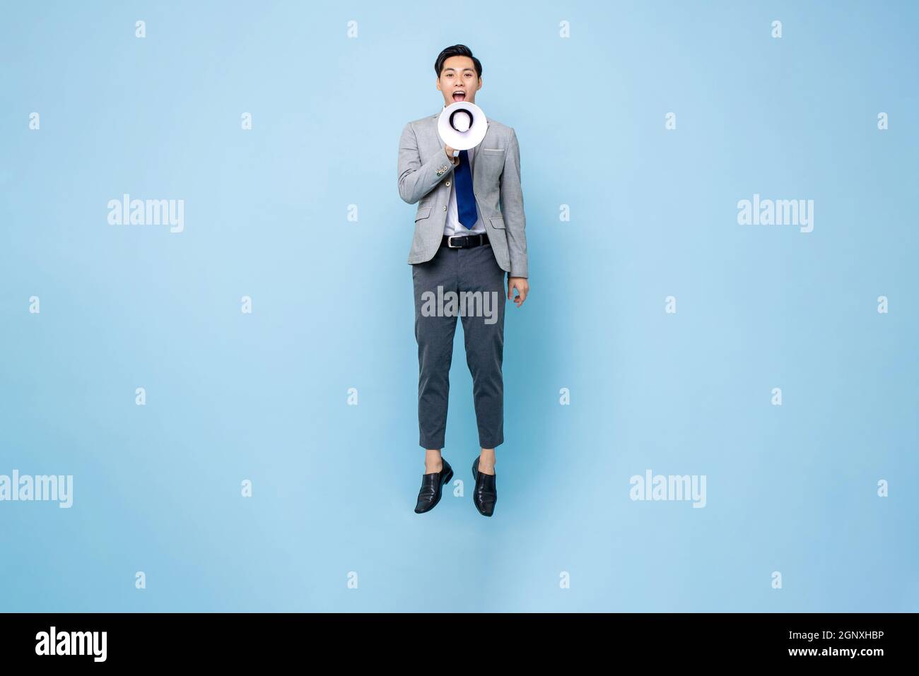 Giovane uomo d'affari asiatico che salta e grida sul megafono isolato su sfondo azzurro Foto Stock
