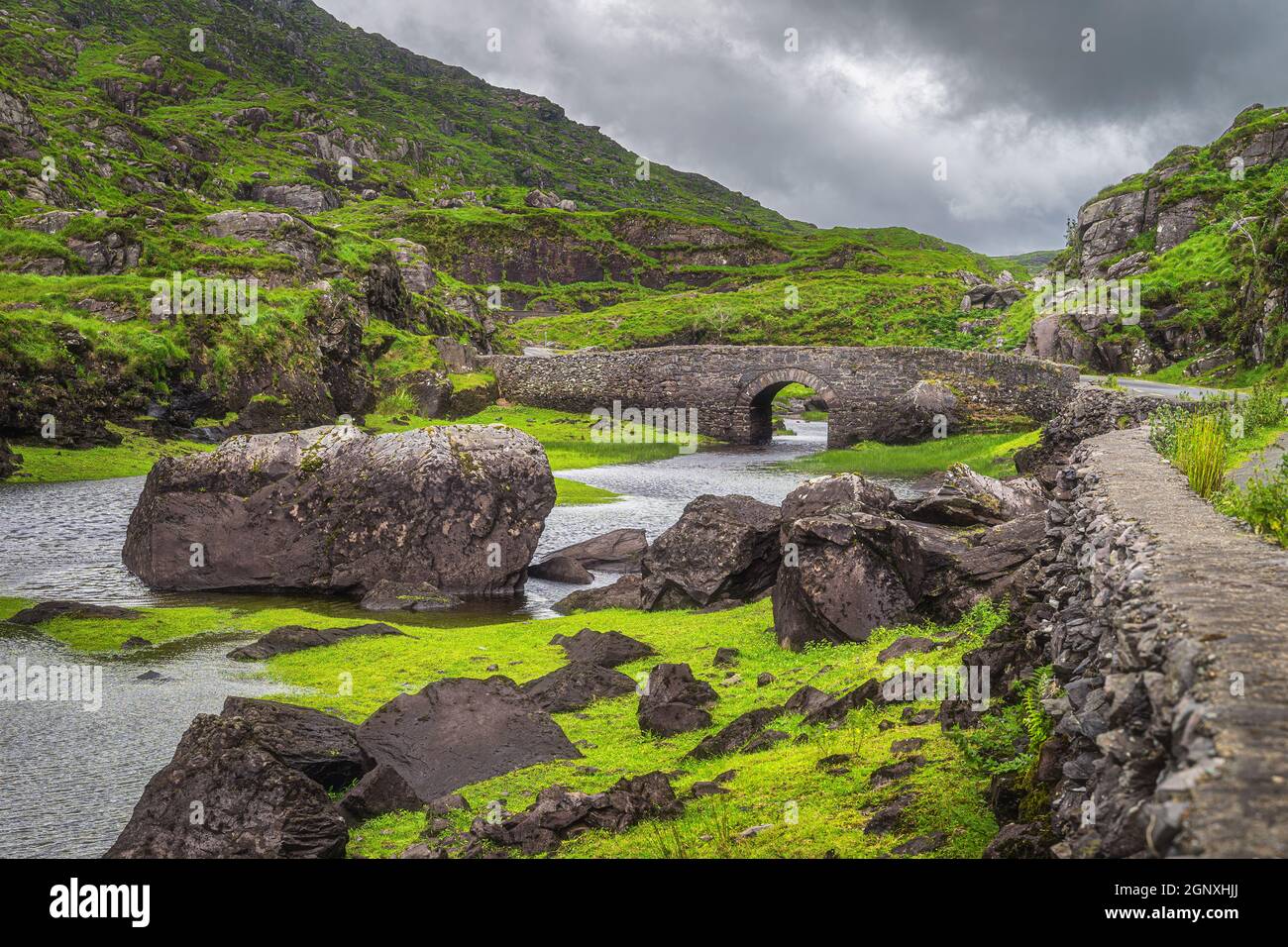 Piccolo ponte di desiderio di pietra sopra il ruscello tortuoso nella valle verde, Gap di Dunloe nella Valle Nera, anello di Kerry, Contea di Kerry, Irlanda Foto Stock