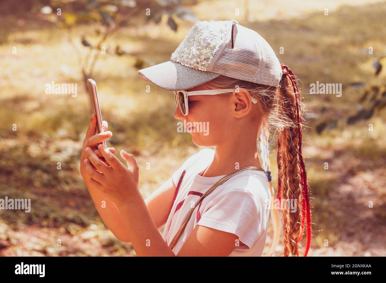Adorabile bambina con lunghi capelli intrecciati in berretto da baseball  con smartphone all'aperto autunno giorno di sole. Stile di vita culturale  giovanile. Testo per i bambini "Happy Traveler Foto stock - Alamy