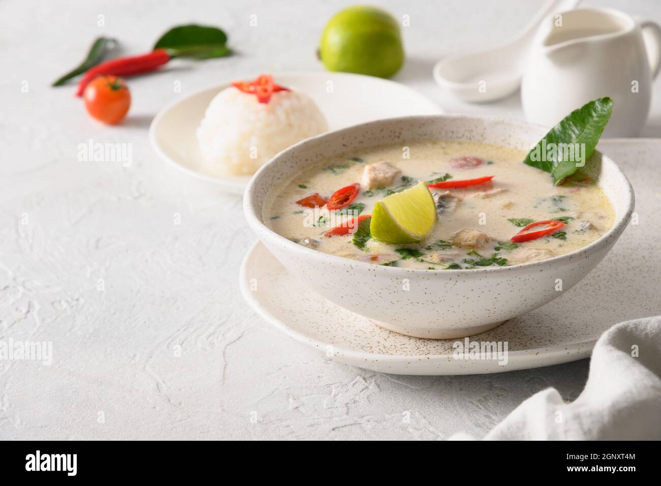 Zuppa cremosa di cocco piccante Tom Kha Gai con pollo, pomodoro ciliegia, latte di cocco, kaffir, galangal, limongrass, funghi su sfondo chiaro. Asia Tha Foto Stock