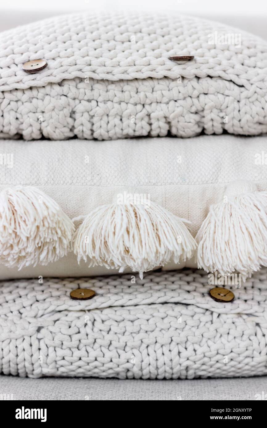 Un mucchio di cuscini in maglia bianca e beige con bottoni e nappine di cotone. Intime texture tessili, interni Hygge e design fatto a mano in casa concetto Foto Stock