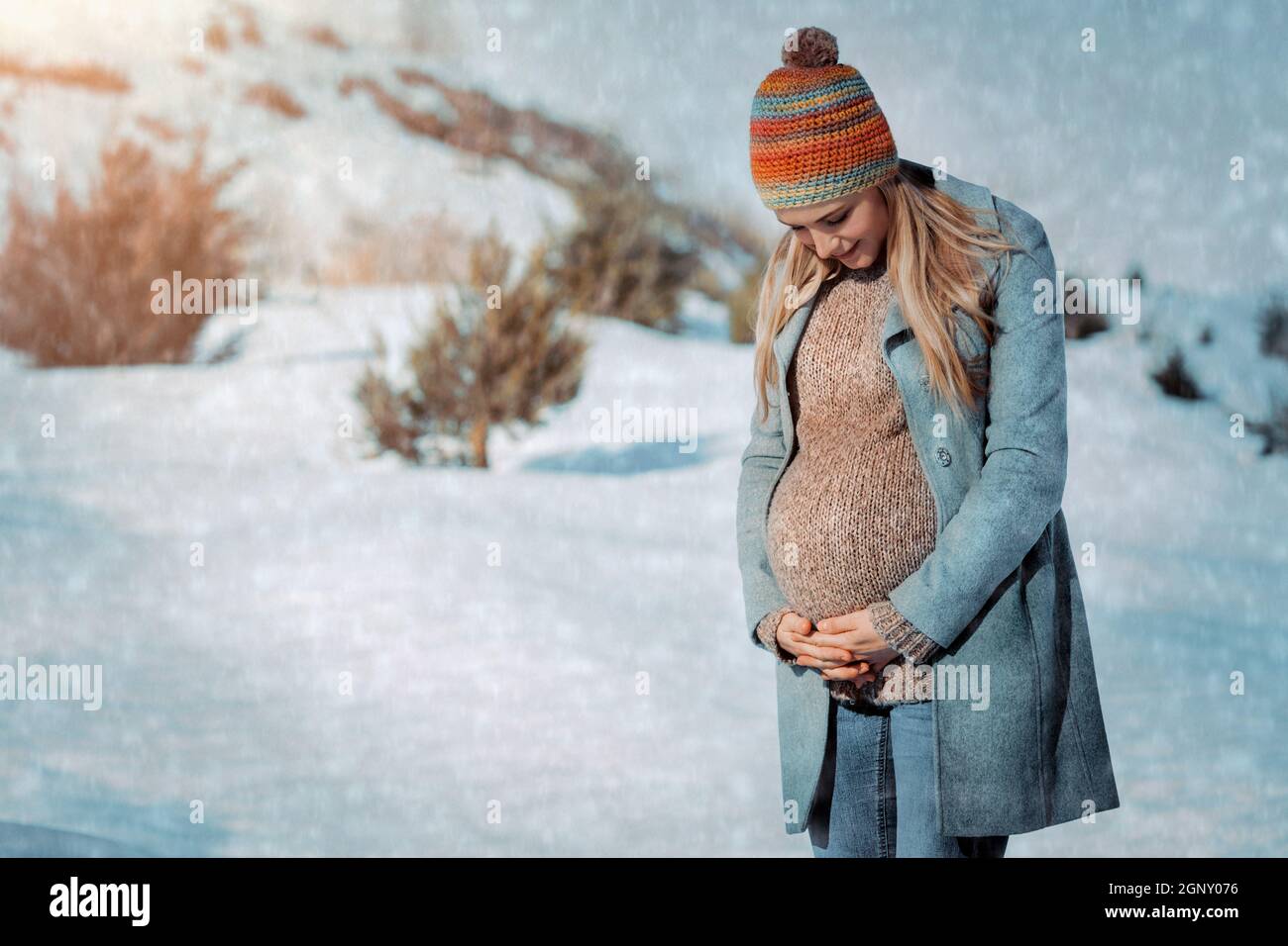 Bella donna incinta Passeggiate in campagna in inverno. Guardando sul pancia e parlando con il bambino. Buona gravidanza. Foto Stock