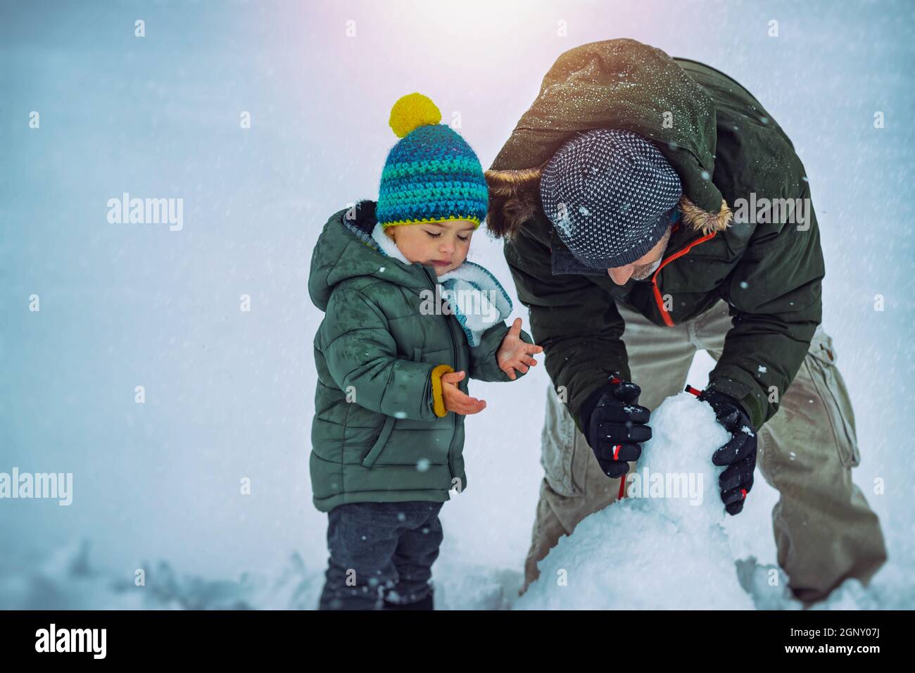 Carino bambino ragazzo con padre che si diverta all'aperto in inverno. Con piacere costruire Snowman. Vacanze invernali insieme. Foto Stock