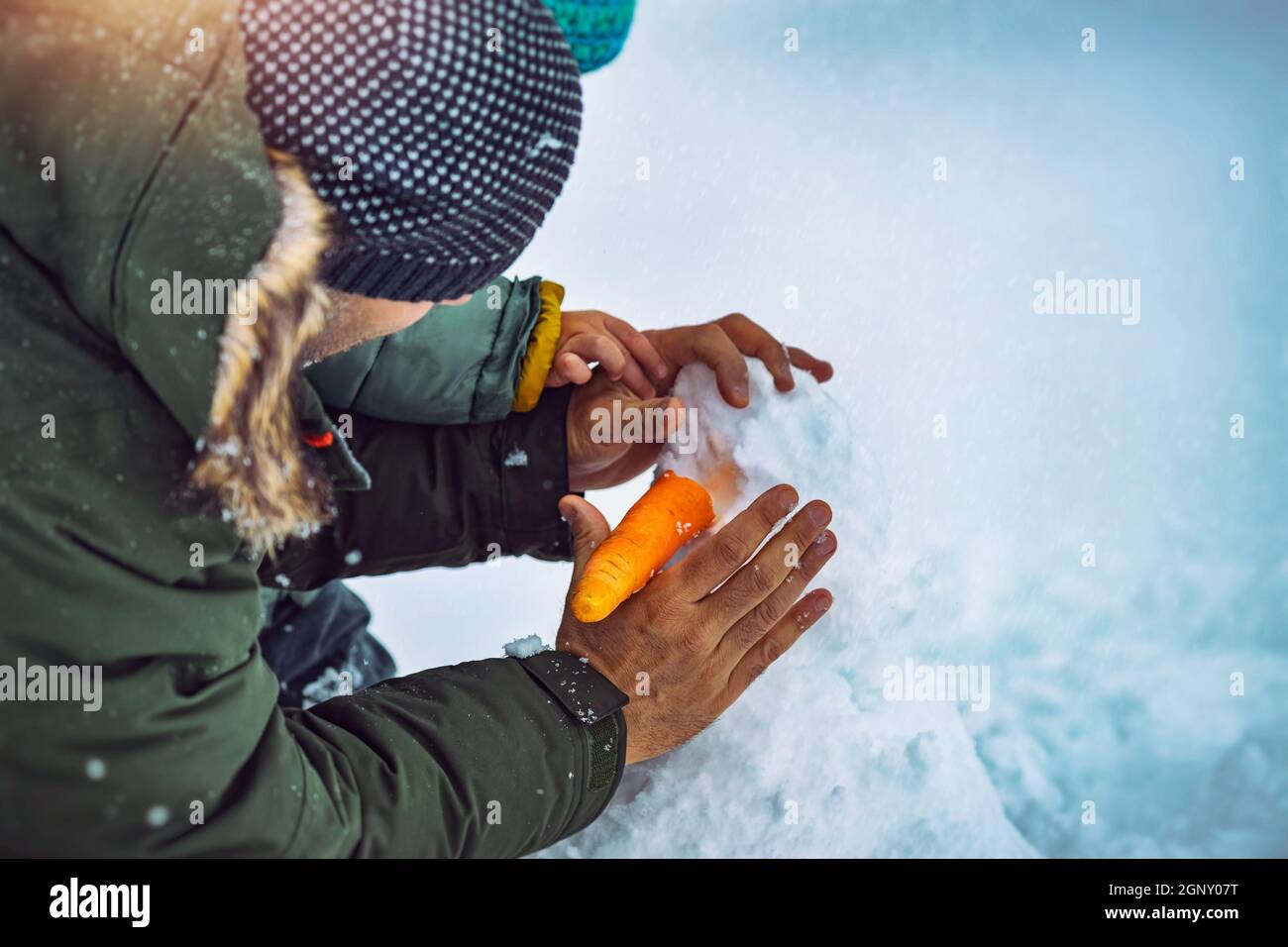 Padre e piccolo Figlio costruendo un pupazzo di neve nel Parco Snowy. Mettere una carota invece del naso. Gioia invernale tradizionale. Buone feste di Natale. Foto Stock