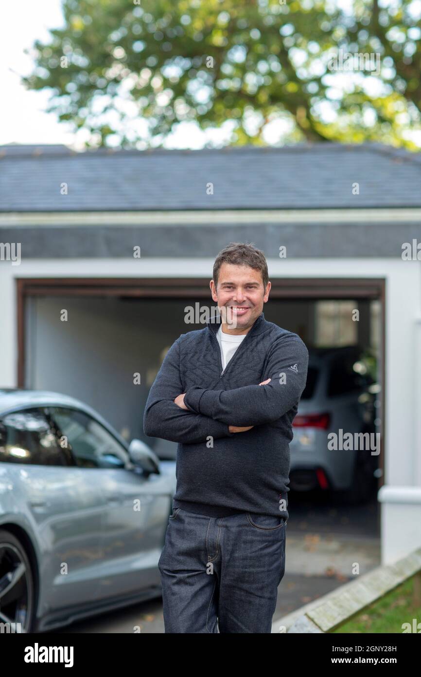 maschio con le sue auto elettriche di fronte al suo garage casa Foto Stock