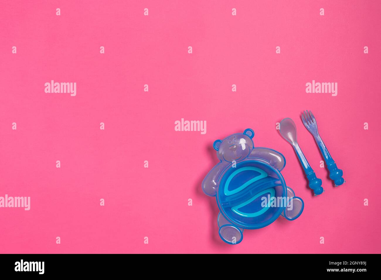Piatto blu bambino con cucchiaio e forchetta isolati su rosa. Vista dall'alto Foto Stock