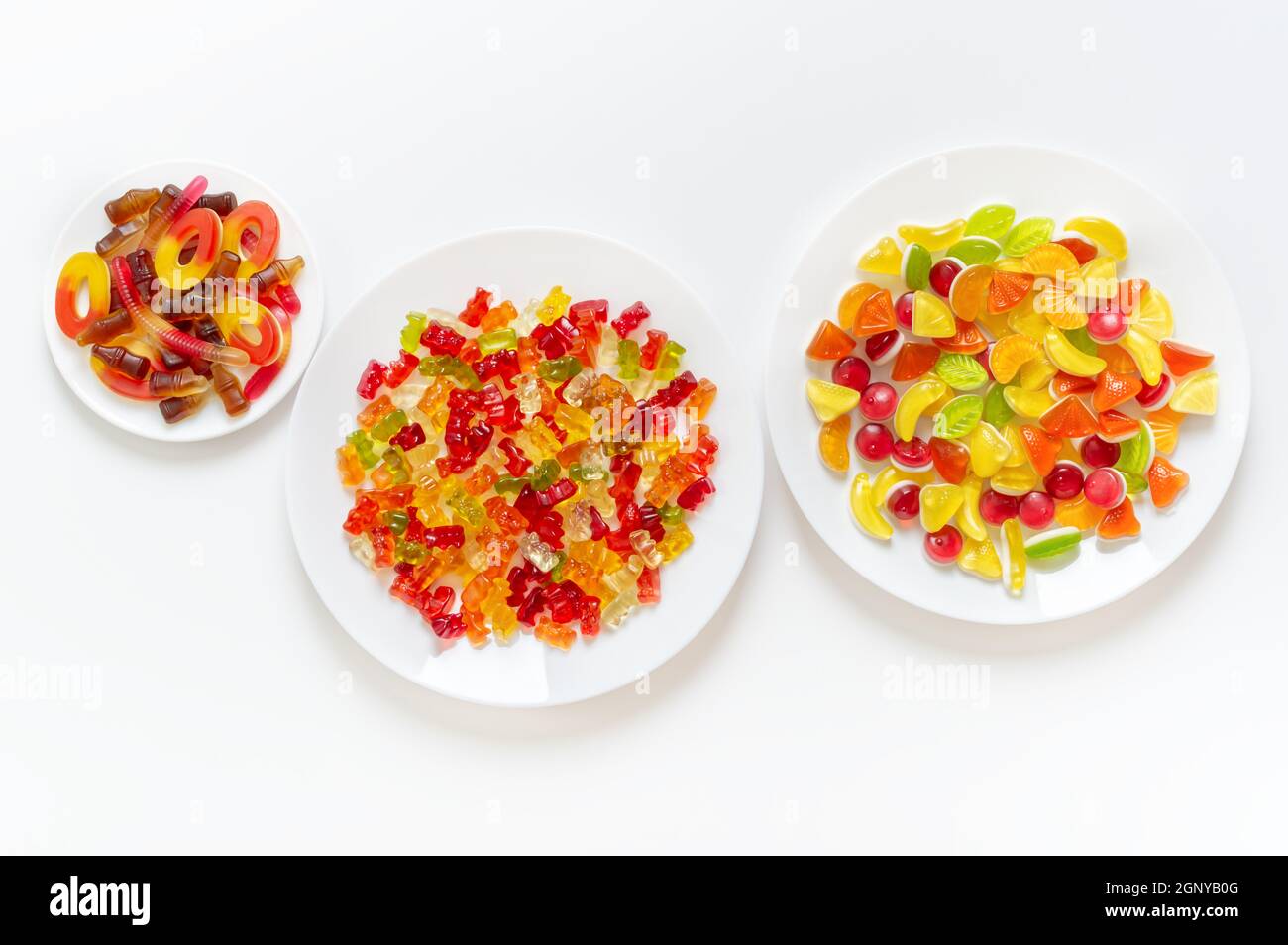 Assortimento di caramelle gelatinose su piatti su sfondo bianco. Caramelle gommose, vista dall'alto. Foto Stock