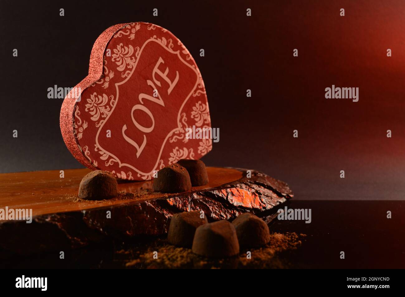 Una scatola rossa a forma di cuore e alcuni sottili tartufi di cioccolato sciolti. Foto Stock