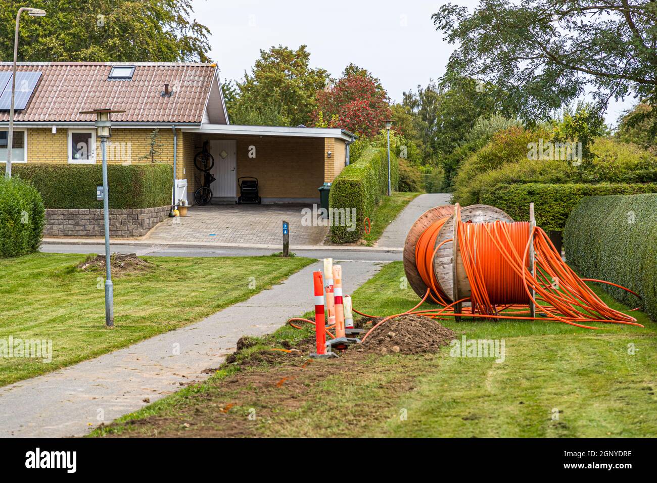 A Tullebølle c'è più progresso di quanto il nome suggerisca: i cavi in fibra ottica vengono posati davanti a ogni casa di questo villaggio sonnolento a Langeland, in Danimarca. Un bobina di cavo con un condotto arancione giace davanti a un carport. Foto Stock
