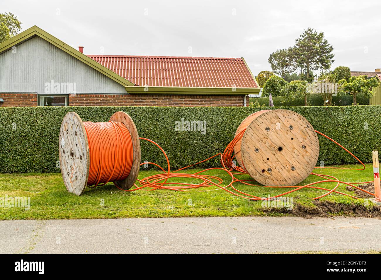 A Tullebølle c'è più progresso di quanto il nome suggerisca: i cavi in fibra ottica vengono posati in ogni casa di questo sonnolento villaggio di Langeland, in Danimarca, raggiungendo persino l'ultima fattoria qui. Due bobine di cavo giacciono davanti a una siepe. Foto Stock
