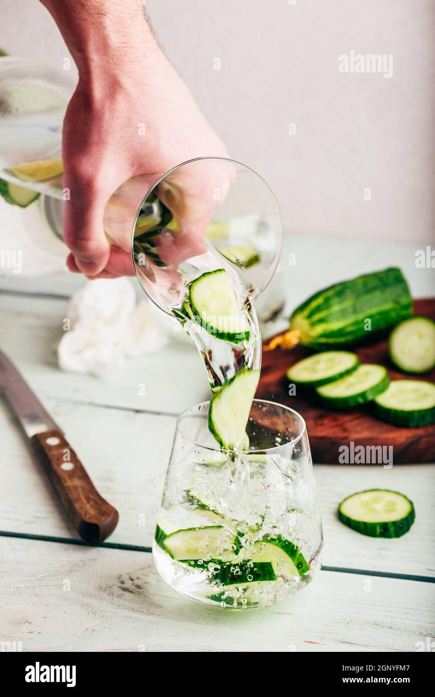 Mano con caraffa versa acqua detox con fette di cetriolo Foto Stock