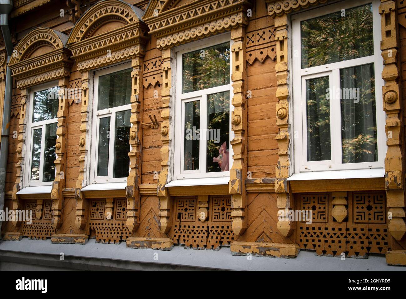 Vecchia casa storica in legno in stile russo con platbands intagliati e una statuetta di un maiale che guarda fuori dalla finestra Foto Stock