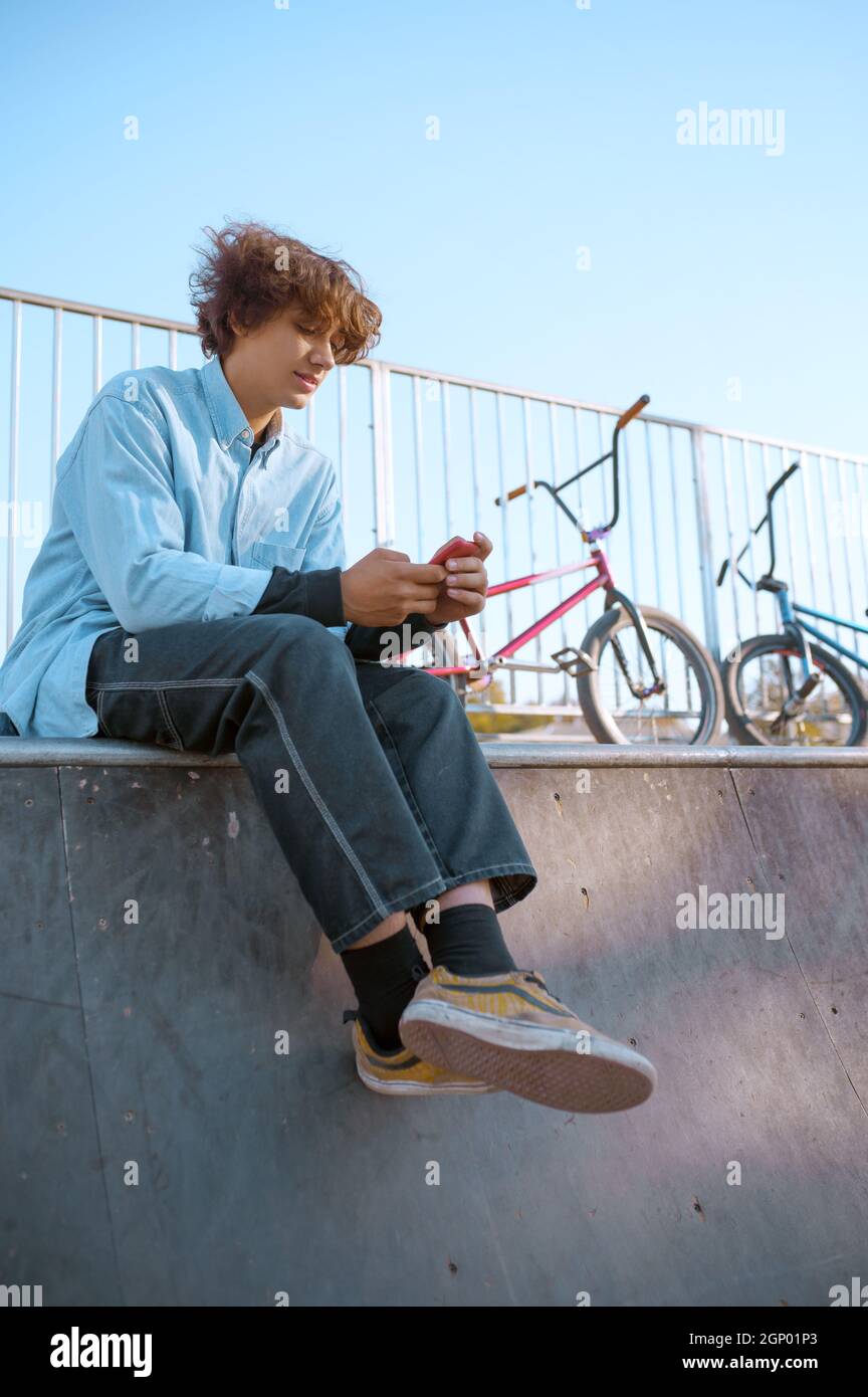 Maschio Bmx biker svaghi sulla rampa in skatepark dopo l'allenamento. Sport estremi in bicicletta, esercizi pericolosi in bicicletta, passeggiate in strada, escursioni in bicicletta nel parco estivo Foto Stock