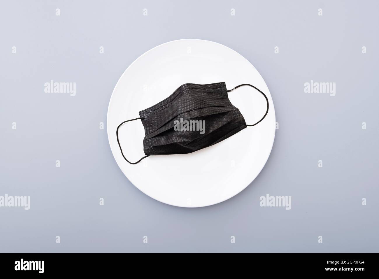 Maschera protettiva nera su piastra in ceramica bianca, vista dall'alto. Concept picture creativo Foto Stock