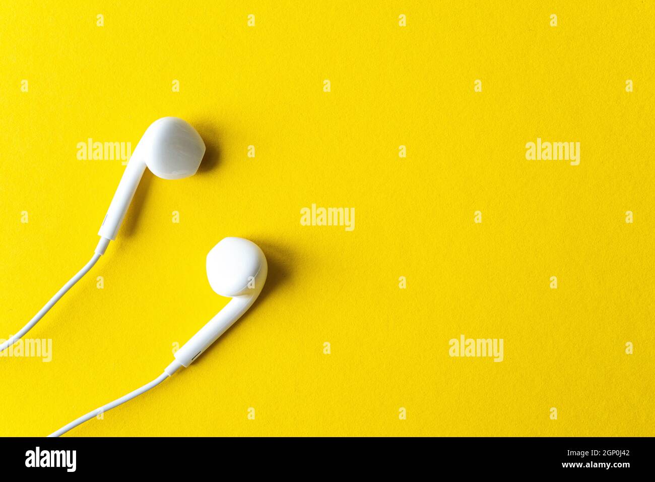 Semplice composizione piatta con cuffie bianche su sfondo giallo chiaro, vista dall'alto, spazio per testo o idee Foto Stock
