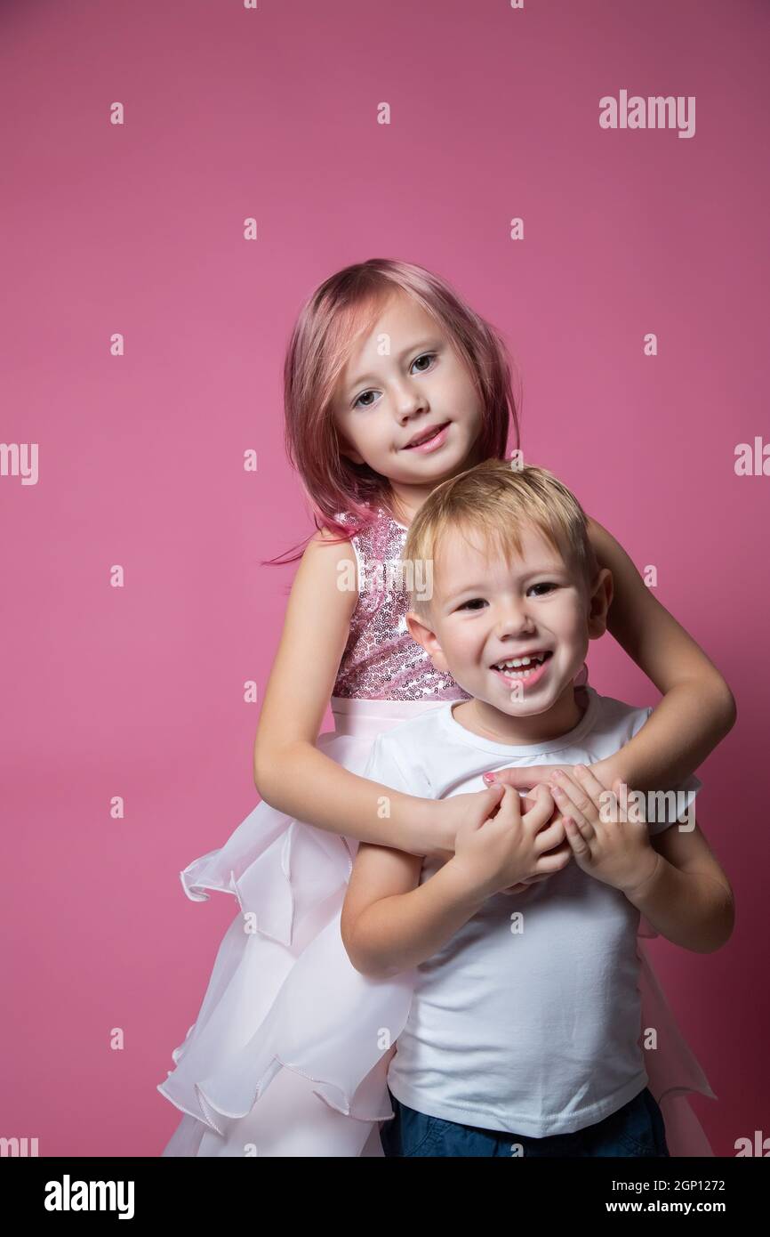 Caucasico fratello e sorella, abbracciando la fotocamera su sfondo rosa studio girato. Foto Stock