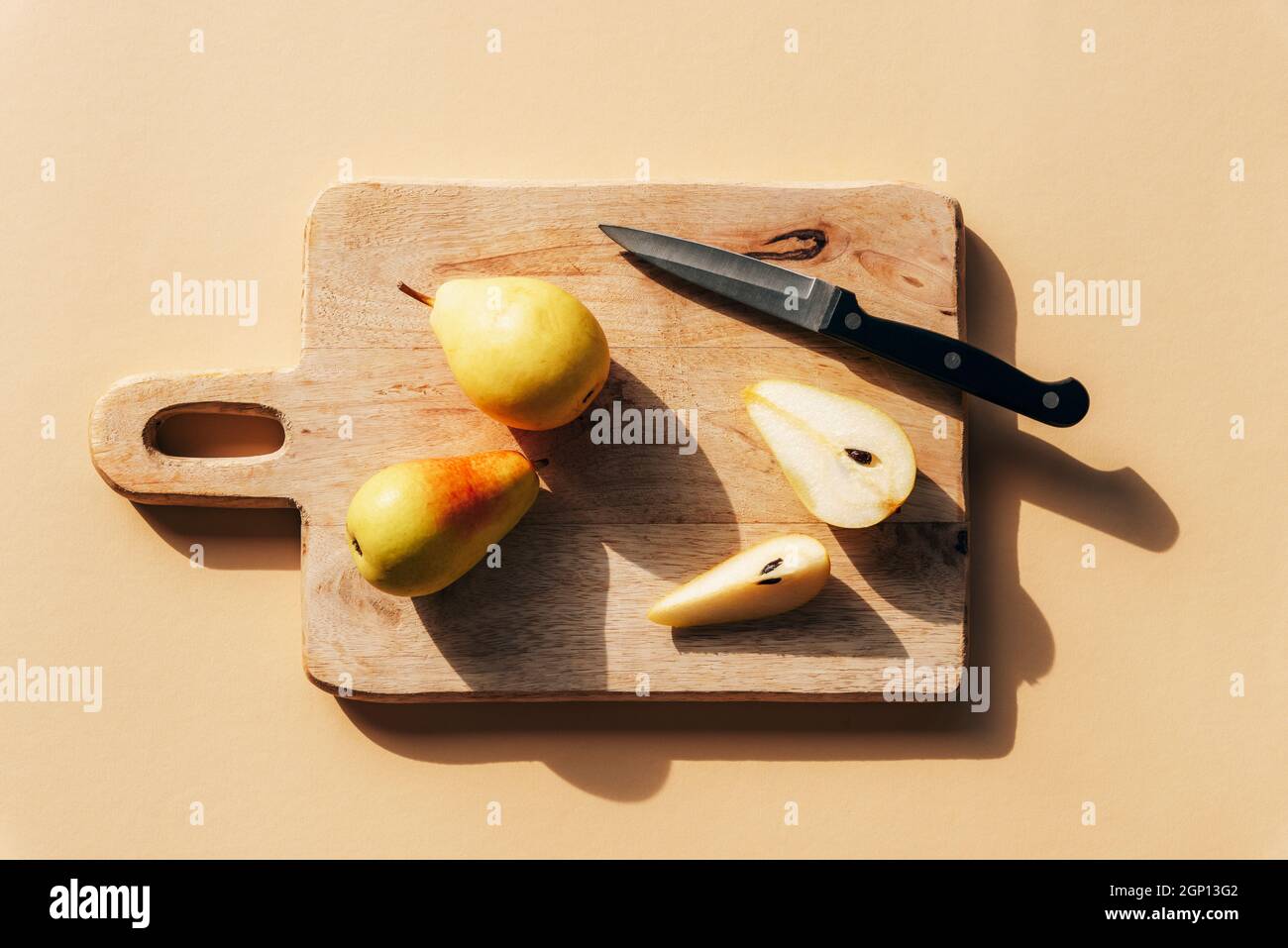 Pere fresche mature e coltello su tagliere di legno sotto la luce del sole. Vista dall'alto, piatto. Foto Stock