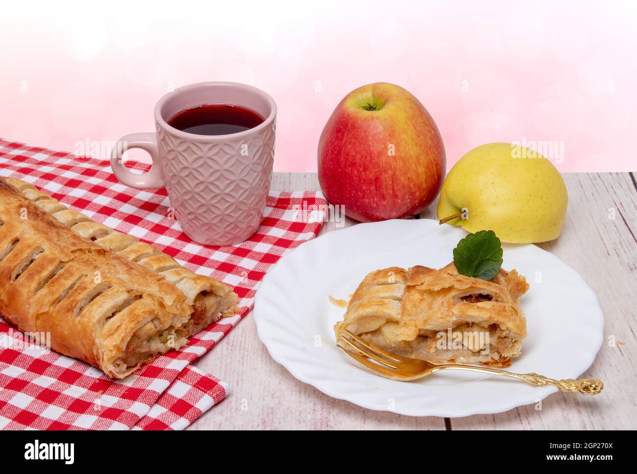 Apple roll servito. Un rotolo di strudel di mele fresco cotto in casa con una tazza di tè, una fetta appetitosa di torta di mele sul piatto e mele fresche su un Foto Stock