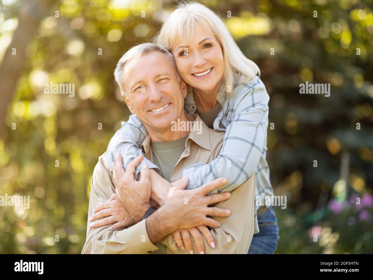 Uomo e donna anziani felici che trascorrono del tempo insieme, abbracciando, riposando in giardino al sole della giornata autunnale all'aperto e sorridendo alla macchina fotografica, spazio copia Foto Stock