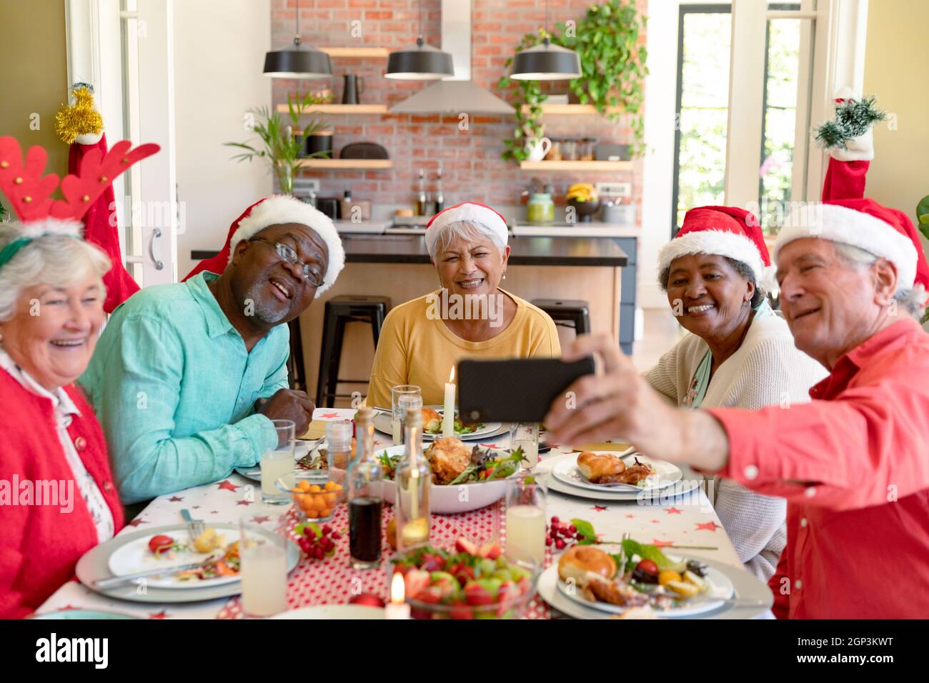 Gruppo vario di amici anziani felici in cappelli di festa che celebrano il natale insieme, prendendo selfie Foto Stock