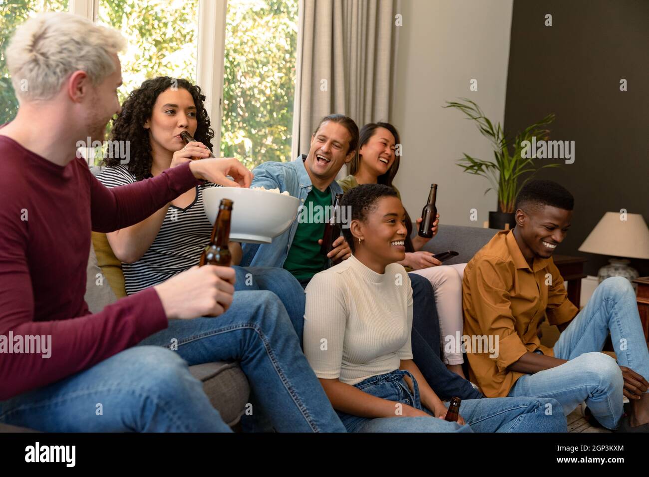 Gruppo di amici allegri e diversi di sesso maschile e femminile che guardano la tv e bevono birra insieme a casa Foto Stock