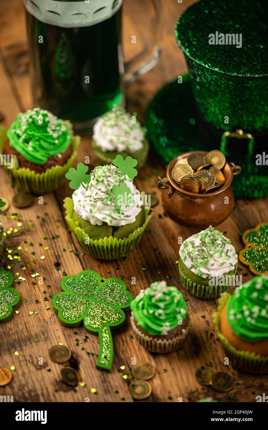 Cupcake decorati e pentola con monete d'oro su tavolo di legno. Festa di San Patrizio Foto Stock