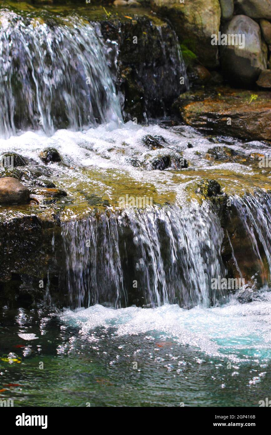 Un laghetto in giardino supporta un multi-tiered cascata con molti strati di lastre di roccia. Foto Stock