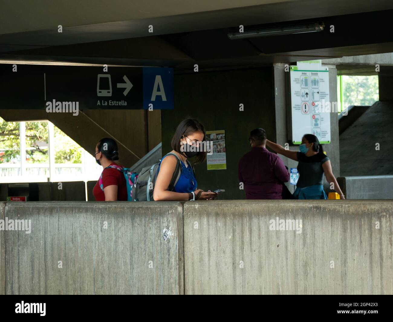 Medellin, Antioquia, Colombia - Settembre 12 2021: La donna indossa una maschera nera protettiva mentre usa il suo telefono e aspetta in una stazione della metropolitana Foto Stock